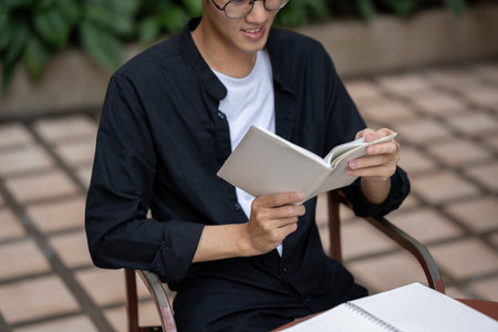Cropped image of a happy Asian man is reading a book or checking his schedule in his planner book at...
