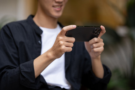 Cropped image of a young Asian man using his smartphone, playing a mobile game or watching a video...