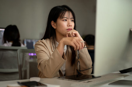 A dissatisfied Asian businesswoman or female office worker is reading emails, looking at her computer screen with a serious face, working in the office.の写真素材