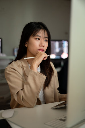 Young concentrated Asian businesswoman or female office employee is working in the office, looking at her computer screen, planning her project.の写真素材