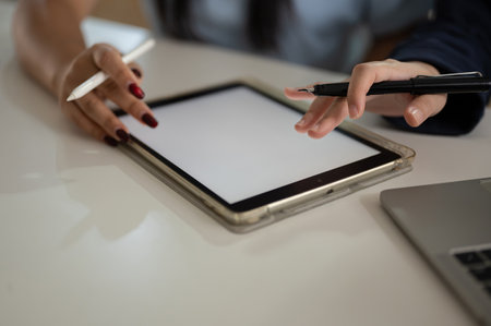Cropped shot of two Asian women are discussing work and using a digital tablet to plan their project in the office together. people and technology conceptsの写真素材