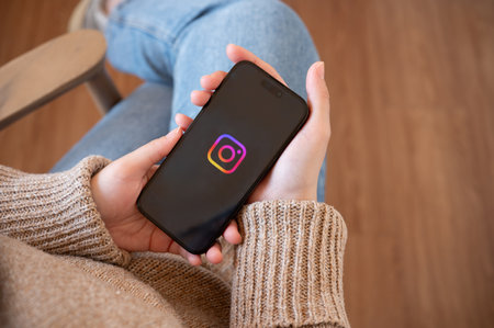 Chiang mai, Thailand - Jan 25 2024: A woman holding an iPhone with Instagram logo on the screen. A woman is login on Instagram application on her smartphone while relaxing indoors.のeditorial素材