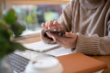 Cropped shot of a woman in a cosy knitted sweater using her smartphone at a table at a cafe co-working space. people, technology, and lifestyle conceptsの写真素材