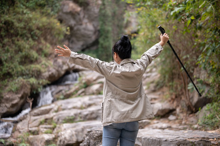 Back view image of a fun, excited Asian woman raising hands and admiring beautiful views of the landscape, enjoying hiking alone on the mountain. nature adventure, girl explorer, travelの写真素材