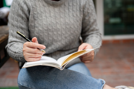 A close-up image of a woman keeping her diary or writing something in her notebook while sitting...