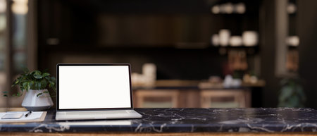 A modern home office features a white-screen laptop computer mockup and accessories on a black marble desk, with a blurred background of a modern black kitchen. 3d render, 3d illustrationの写真素材