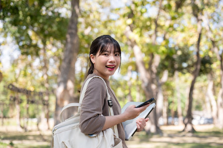 An attractive young Asian female college student with a backpack is walking in the campus park on a bright day. university life conceptの写真素材