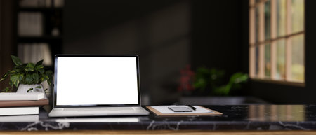 A modern workspace with a white-screen laptop mockup, a smartphone, documents, books, and a potted plant on a black marble table in a modern black room. 3d render, 3d illustrationの写真素材