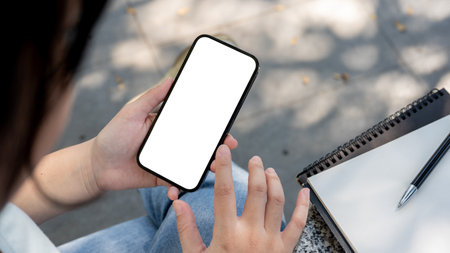 A close-up shot of an Asian woman using her smartphone while sitting at an outdoor table. a...