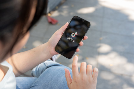 Chiang Mai, Thailand - Feb 02 2024: A close-up shot of a woman using the TikTok application on her iPhone while sitting outdoor.のeditorial素材