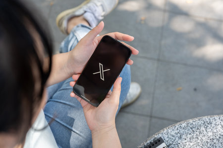 Chiang Mai, Thailand - Feb 02 2024: A close-up shot of a woman using the X application on her iPhone while sitting outdoor. X application, new Twitterのeditorial素材