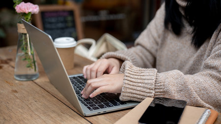 Cropped shot of a woman in a cosy sweater working remotely at a cafe in the city, working on her...