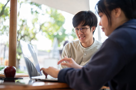 Two Asian colleagues are focusing on their project on a laptop, discussing and sharing ideas, while working remotely at a cafe in the city.の写真素材