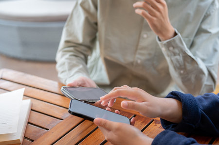 A cropped shot of two people sharing contact info or transferring files by bringing two smartphones...