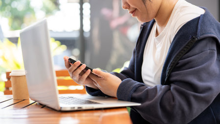 A cropped shot of an Asian female freelancer multitasking, using her smartphone while working...