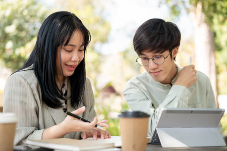Two Asian male and female colleagues are discussing and collaborating on work together at a cafe. working remotely and teamwork conceptsの写真素材
