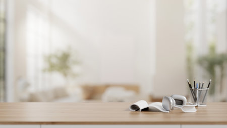 A wooden table with a book, a headphone, a pencil stand, and an empty space for display product with a blurred background of a modern white living room. 3d render, 3d illustrationの写真素材