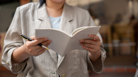 A cropped shot of a businesswoman holding her notebook and taking notes in it, listing her ideas.