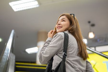 An attractive, positive Asian female tourist with her luggage is on an escalator in the airport,...