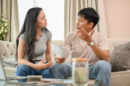 Unhappy, stressed Asian spouses are sitting on a couch, arguing about unexpected high household bills and credit card invoices. family bankruptcy, debt, lack of financesの写真素材