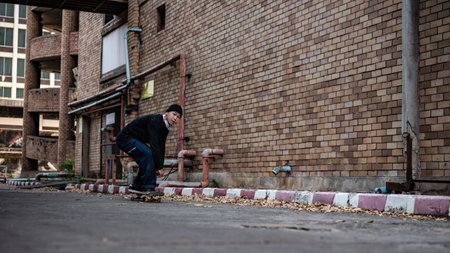 A cool, active Asian skater guy in stylish hipster clothes is riding a skateboard on the street, enjoying riding a skateboard outdoors.の写真素材