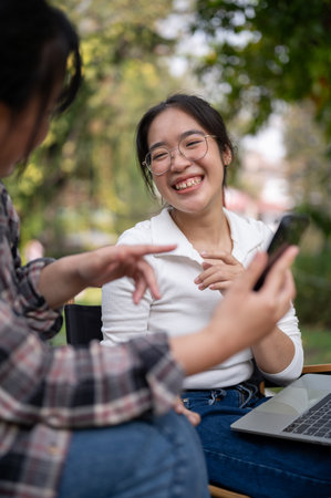 A cheerful Asian woman is enjoying talking with her friend while sitting in a green backyard garden...