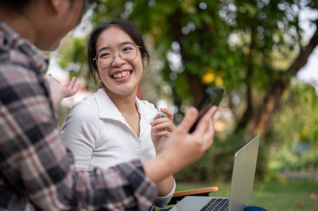 A cheerful Asian woman is enjoying talking with her friend while sitting in a green backyard garden together. people and lifestyle conceptsの写真素材