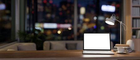 A white-screen laptop computer mockup on a wooden desk in a contemporary home office at night illuminated by dim lights from a table lamp. close-up image. 3d render, 3d illustrationの写真素材