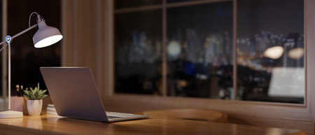 A laptop computer on a wooden desk in a contemporary room at night, with a view of the city...