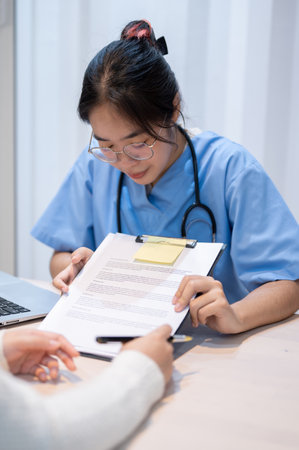 A professional Asian female doctor showing a medical checkup form or explaining a medical insurance claim document to a patient during a meeting in the office. healthcare conceptの写真素材