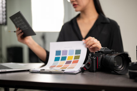 A close-up image of a professional DSLR camera on a desk in a studio, a female photographer is checking color on a color checker. selective focusの写真素材