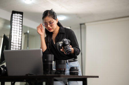 An attractive, professional Asian female photographer is checking images on her laptop, working in a...