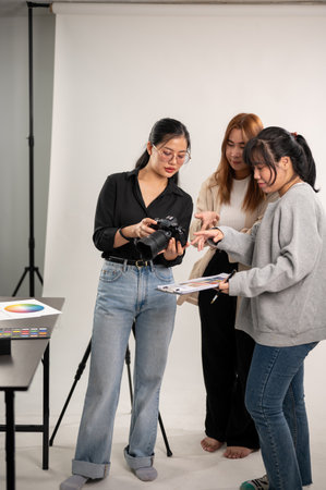 A cool, professional Asian female photographer is talking and showing images on the camera to her team, working in the fashion shooting studio, and briefing the concept with an art director.の写真素材