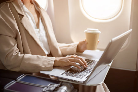 A cropped image of a hard-working businesswoman in a business suit is working on her laptop computer during the flight, flying to another city for a business meeting. working remotely, airplane modeの写真素材