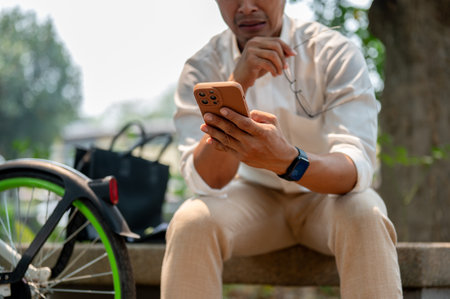 A cropped image of a sad Asian millennial businessman sits outdoors on a bench with bicycle rests...