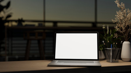 A laptop computer white-screen mockup on a wooden desk under dim light in a contemporary dark co-working space at night. dark workspace concept. close-up image. 3d render, 3d illustrationの写真素材