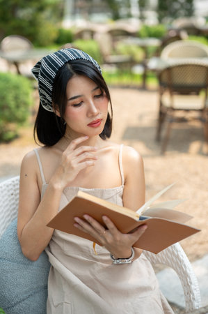 A beautiful Asian woman in a cute dress relaxes in a beautiful garden on a bright day, reading a book. leisure, hobby, lifestyleの写真素材