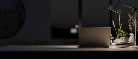 A modern dark office at night features a laptop computer, decorative objects, and a dim light from a table lamp on the table. close-up image. 3d render, 3d illustrationの写真素材