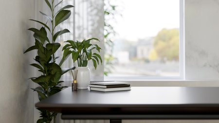 A close-up image of a table near the window featuring a reed diffuser, books, and decorative plants...