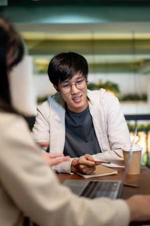 A young, smart Asian male college student is having a meeting with his friend in a cafe to discuss...