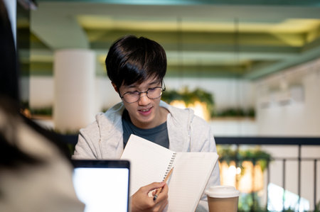 A young, smart Asian male college student is tutoring, helping his friend with math homework, discussing a co-project, or preparing for an exam together in a cafe co-working space.の写真素材