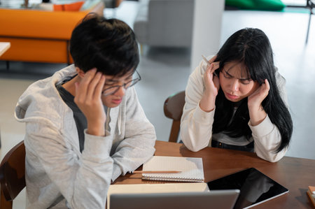 Two frustrated young Asian college students are sitting in a cafe or co-working space, having a problem with their project and arguing while working together.の写真素材