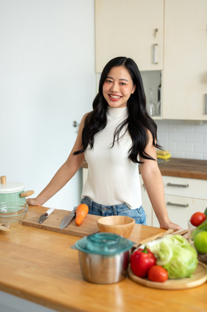 An attractive young Asian woman stands at the kitchen table in the kitchen and smiles at the camera, going to make her healthy breakfast. home cooking, healthy lifestyleの写真素材