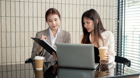 Two attractive Asian businesswomen or female office workers are checking the documents, having a meeting, discussing work, and working on an assignment together in the meeting room.の写真素材