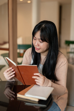 A beautiful, positive Asian woman enjoying reading a book in a beautiful coffee shop. people,...
