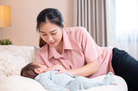 A beautiful, caring young Asian mom is comforting and putting her newborn baby son to sleep in the...