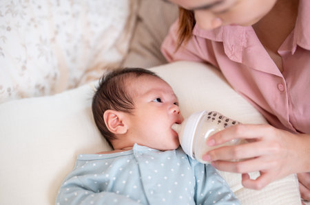 An Asian mom feeing her newborn baby son with a bottle on the bed, putting her baby to sleep....