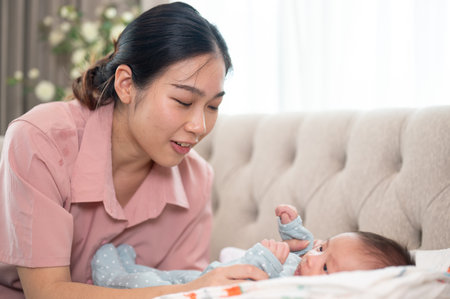 A happy young Asian mom comforting her newborn baby son to sleep on the couch together in the living room. motherhood, mom's love and tendernessの写真素材