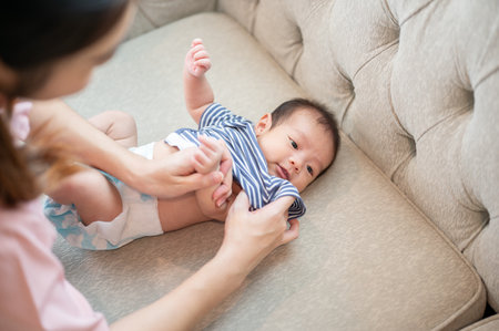 A caring mom is changing her newborn baby's clothes and diaper, or putting on a diaper and pajamas for him on the couch in the living room. childcare and motherhood conceptsの写真素材