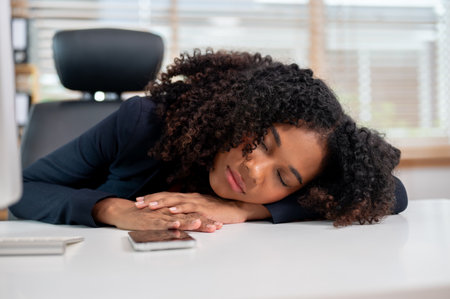 A tired, sleepy Black businesswoman taking a nap at her desk in the office, falling a sleep during work, taking a break on the afternoon.の写真素材
